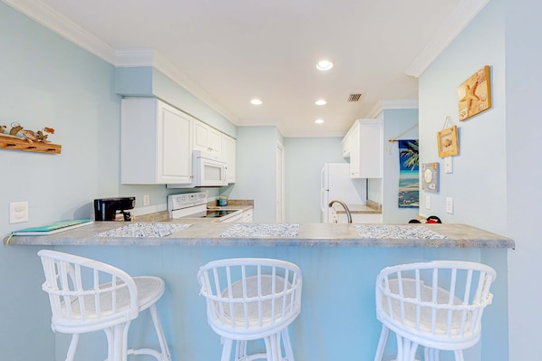 A kitchen with white cabinets, a countertop, and three white bar stools. - Pool-side condo with pool, private washer&dryer, walk to beach & free WiFi (Navarre Beach)