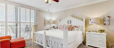 A bedroom with a white bed, a ceiling fan, a nightstand, and a window with blinds.