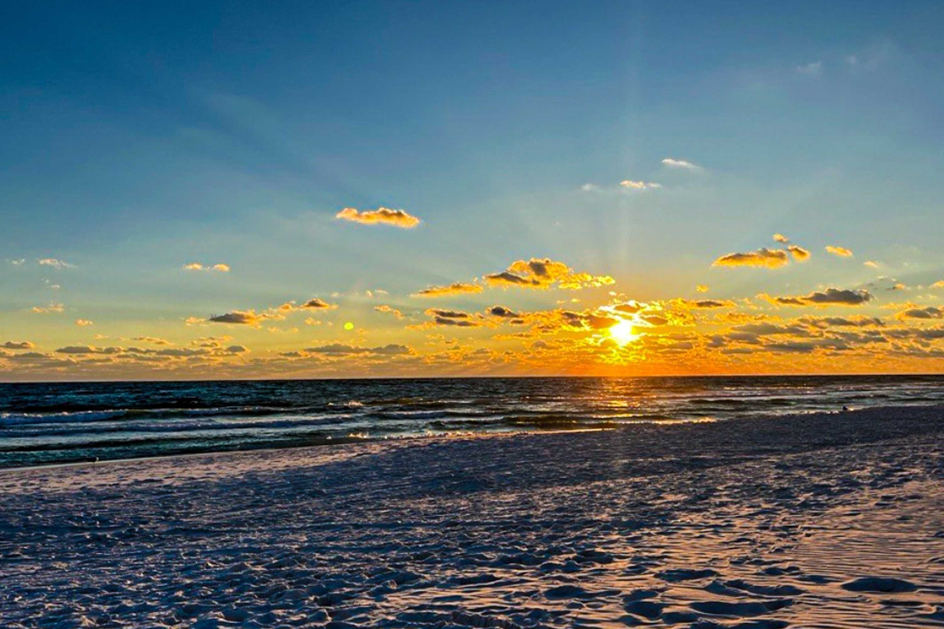 A beach scene with the sun setting over the ocean, creating a silhouette of the shoreline.