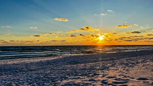 En strandscene med solnedgang over havet, der skaber en silhuet af kystlinjen.