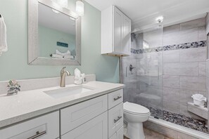 A bathroom with a white sink, a mirror, a toilet, and a shower area. - Sunny condo with lake views, outdoor pool, fast WiFi, tennis & central AC (Miramar Beach)