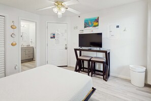 Ein Hotelzimmer mit einem Bett, einem Schreibtisch mit zwei Stühlen, einem Deckenventilator, einem Fernseher und einem Papierkorb.
