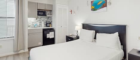 Een hotelkamer met een bed, nachtkastje, bureau met lamp, magnetron en kitchenette.