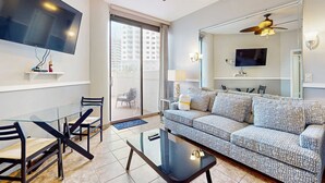 A modern living room with a sofa, a glass coffee table, and a TV mounted on the wall. - Gorgeous ground-floor condo, private patio,  shared pool and beach access (Miramar Beach)