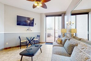 A modern living room with a flat-screen TV, a ceiling fan, a sofa, a coffee table, and a dining area with chairs. - Gorgeous ground-floor condo, private patio,  shared pool and beach access (Miramar Beach)