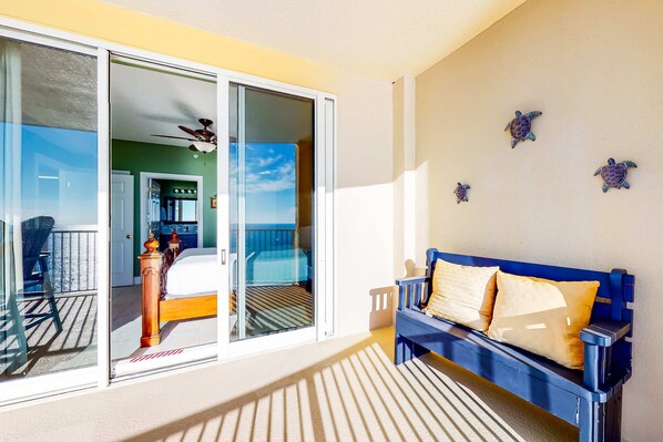 A balcony with a bed, a blue sofa, and decorative turtle wall art. - Ocean-view condo with pool, hot tub, WiFi, AC, & complimentary beach service (Panama City Beach)