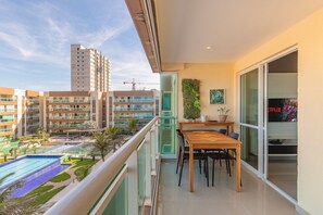A balcony with a view of a swimming pool, a dining area with a table and chairs, and a large window with a plant on the wall. - VG Fun #405 - Praia do Futuro by Carpediem (Fortaleza)