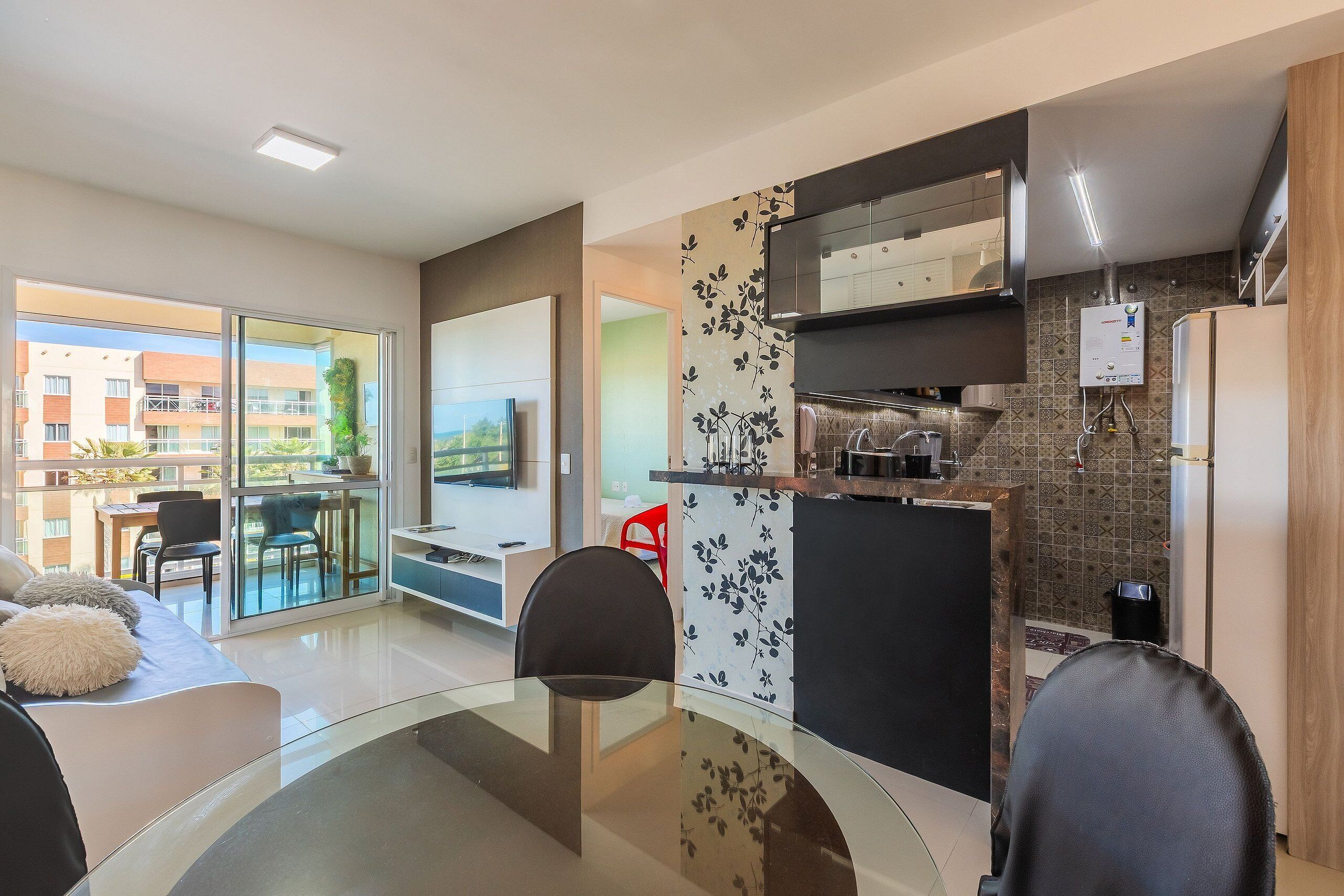 A modern kitchen with a built-in stove, a refrigerator, and a water heater. There is a dining area with a glass table and chairs.