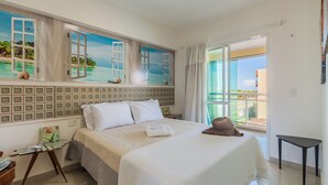 Un dormitorio con una cama grande, una ventana con vistas al mar, una mesita pequeña y una silla.