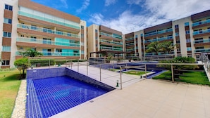 Un hotel moderno con varios balcones, piscina y un jardín bien cuidado.