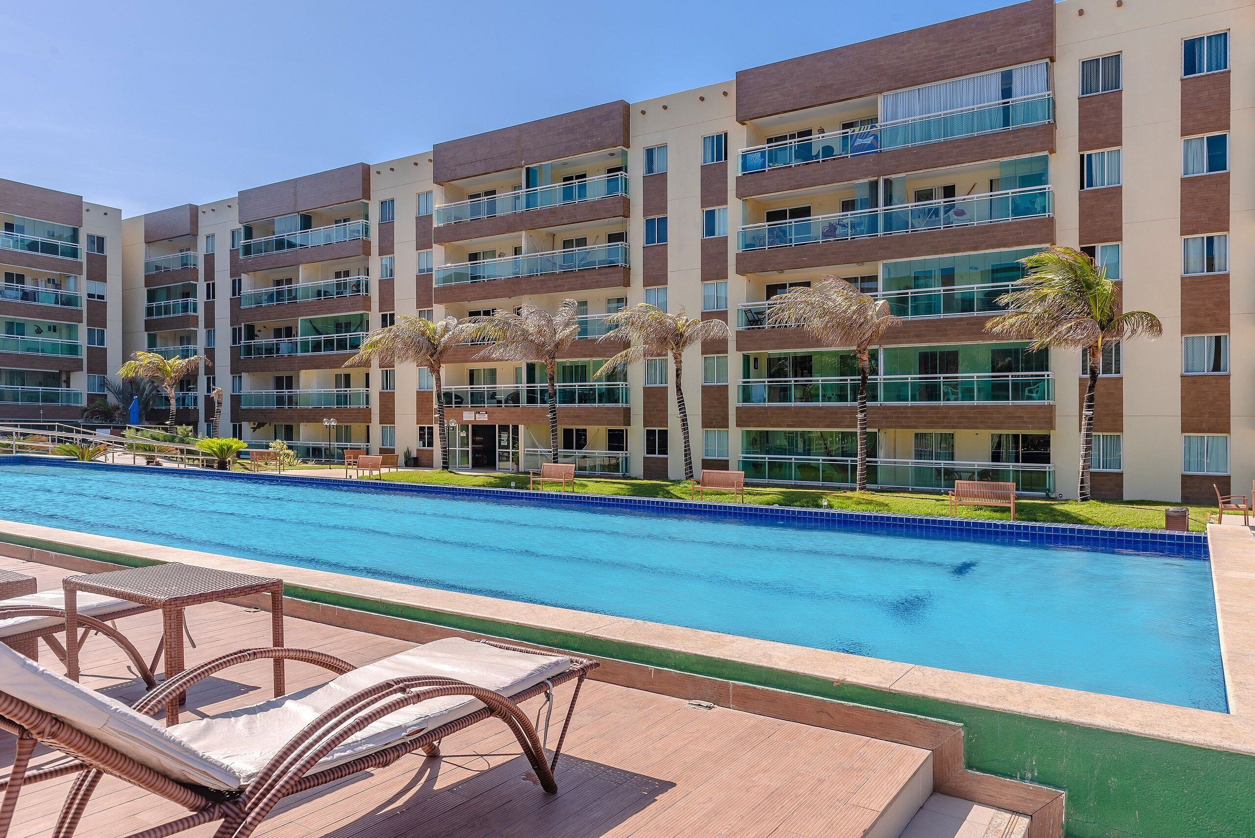 Un hotel con piscina, sillas de descanso y palmeras.