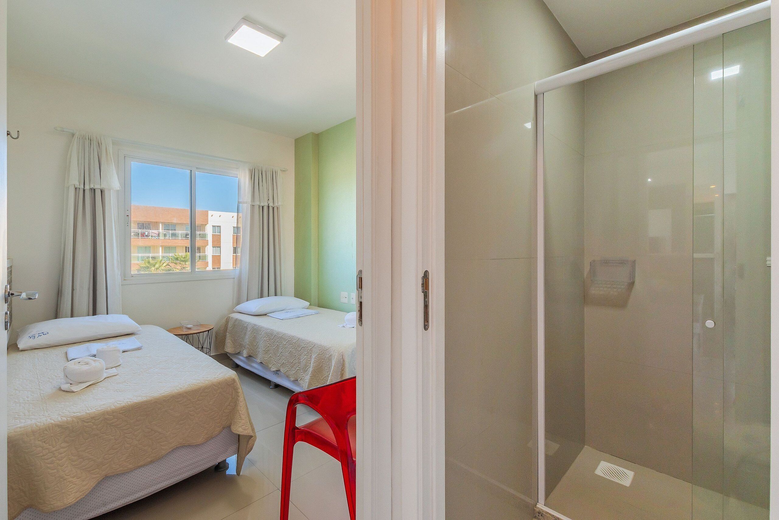 Camera d'albergo con due letti, zona doccia e vista sugli edifici.