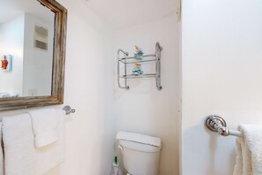 Ein Badezimmer mit Toilette, Handtuchhalter, Spiegel und Ablagefläche mit Dekoration.
