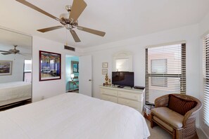 Ein Schlafzimmer mit einem Bett, einem Deckenventilator, einer Kommode mit Fernseher und einem Korbstuhl.