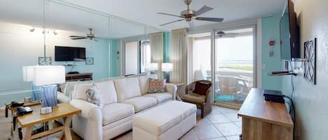 A modern living room with a sofa, ottoman, wooden side table, and a ceiling fan.