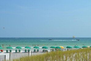 A beach with green umbrellas, a wooden fence, and a clear blue sky.