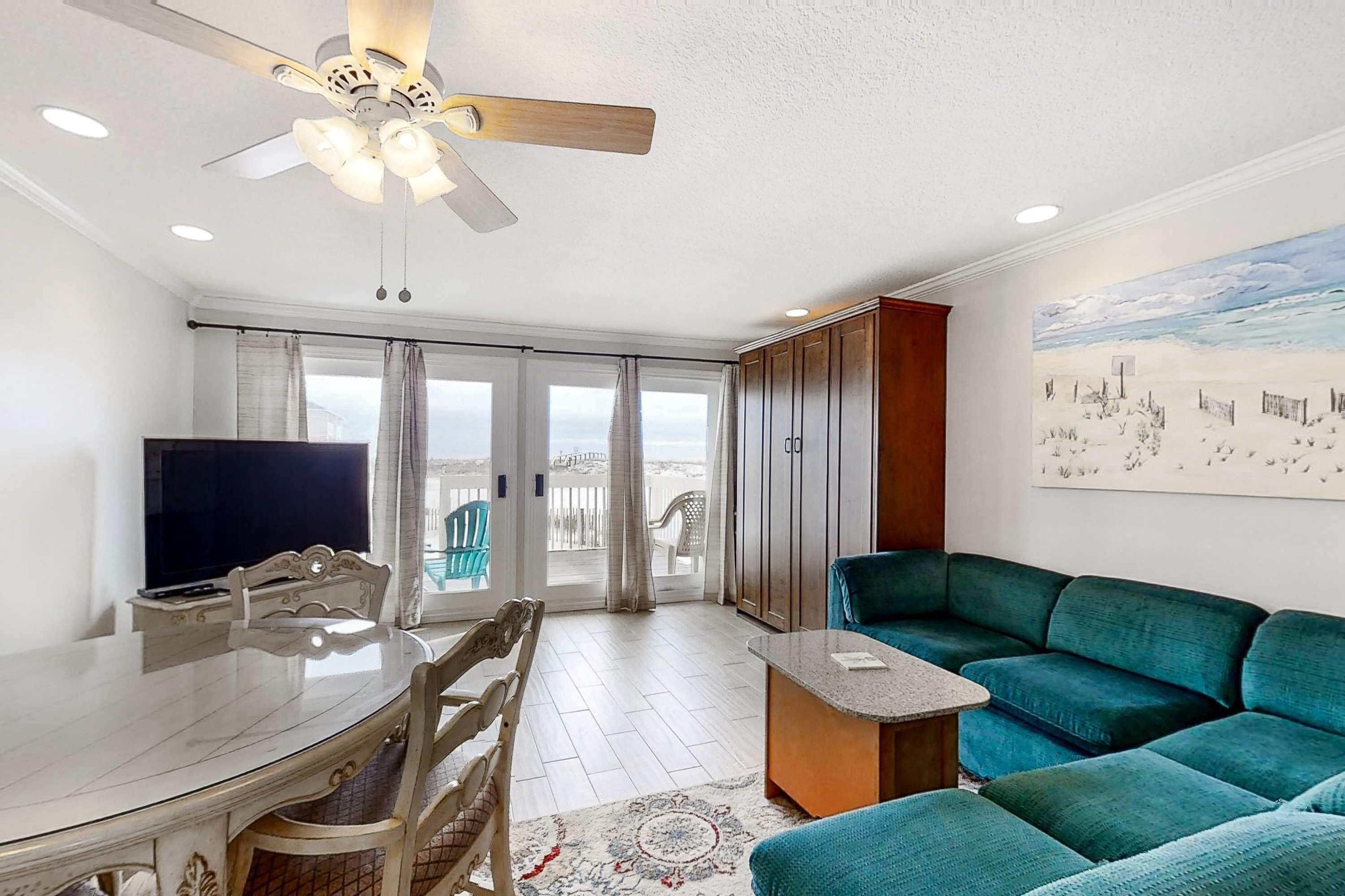 A living room with a TV, a ceiling fan, a sofa, and a dining area with a table and chairs.