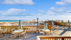 Eine Holzterrasse mit Außenmöbeln und Sonnenschirmen mit Blick auf einen Strand.