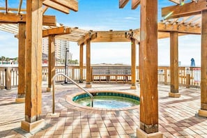 En pergola i træ med et spabad nedenunder, omgivet af en fliseterrasse.