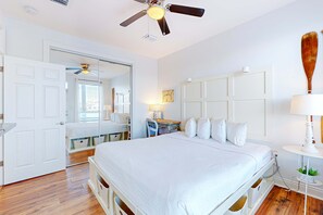 Et soveværelse med seng, skrivebord, stol, ventilator og et spejl.
