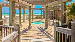 A wooden deck with a pool, wooden pillars, and a view of the beach. - Gulf-view condo at beachfront resort with pools, hot tub & 2 gyms (Destin)