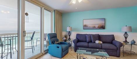 A living room with a sofa, armchair, glass coffee table, and a ceiling fan.