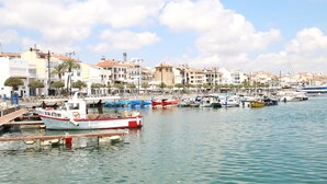 Uma marina com barcos atracados, céu claro e edifícios ao fundo.