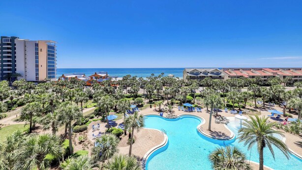 Een resort met een groot zwembad, palmbomen en uitzicht op de oceaan.