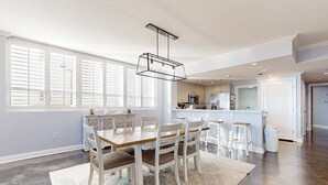 Een moderne keuken met witte kasten, een centraal eiland, en een eethoek met een houten tafel en stoelen.