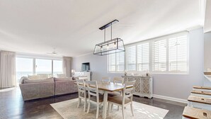 Een ruime woonkamer met een groot raam, een eethoek met een houten tafel en stoelen, en een moderne plafondlamp.
