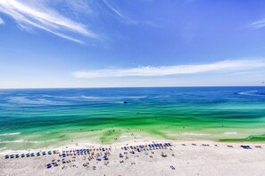 A beach with clear turquoise waters, a sandy shore, and numerous umbrellas. - 20th-story condo in Pelican Beach Resort with Gulf views (Destin)