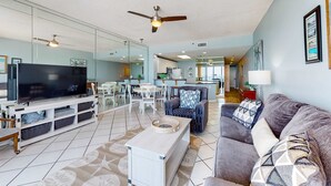 A spacious living room with a flat-screen TV, a ceiling fan, and a dining area in the background. - Cozy condo with Gulf-front balcony & great views - near shops & dining (Destin)