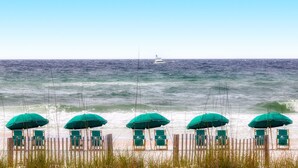 A beach with rows of green umbrellas and beach chairs, a wooden fence, and a boat in the distance. - Cozy condo with Gulf-front balcony & great views - near shops & dining (Destin)