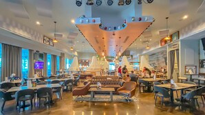 A spacious hotel lobby with a central seating area, multiple dining tables, and a modern ceiling design. - Beachy resort condo with balcony, outdoor pools, hot tub, gym, tennis, AC, & W&D (Destin)