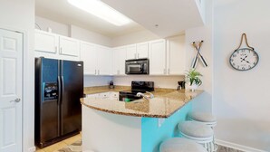 A kitchen with white cabinets, a black refrigerator, a microwave, a sink, and a clock on the wall. - Beachy resort condo with balcony, outdoor pools, hot tub, gym, tennis, AC, & W&D (Destin)