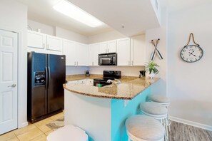 A kitchen with white cabinets, a black refrigerator, a microwave, a sink, and a clock on the wall. - Beachy resort condo with balcony, outdoor pools, hot tub, gym, tennis, AC, & W&D (Destin)