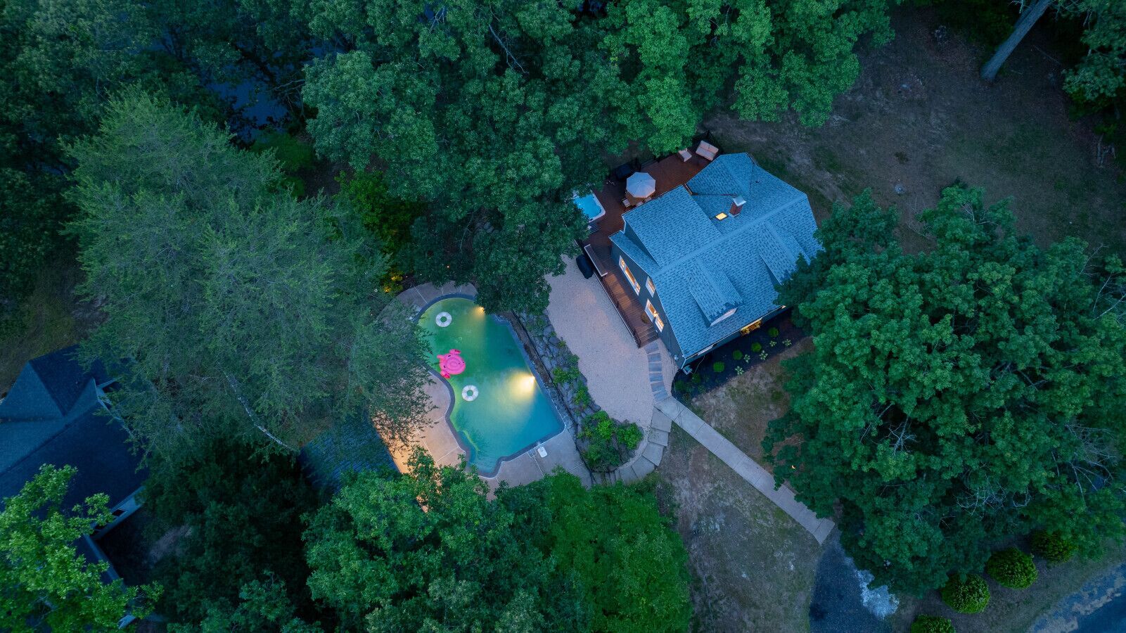 An aerial view of a house with a swimming pool, surrounded by dense trees.