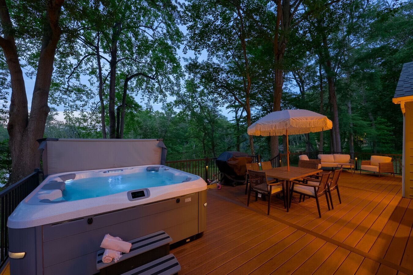 Un jacuzzi en una terraza de madera con mobiliario exterior y una sombrilla.