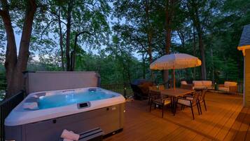 Un jacuzzi en una terraza de madera con mobiliario exterior y una sombrilla.