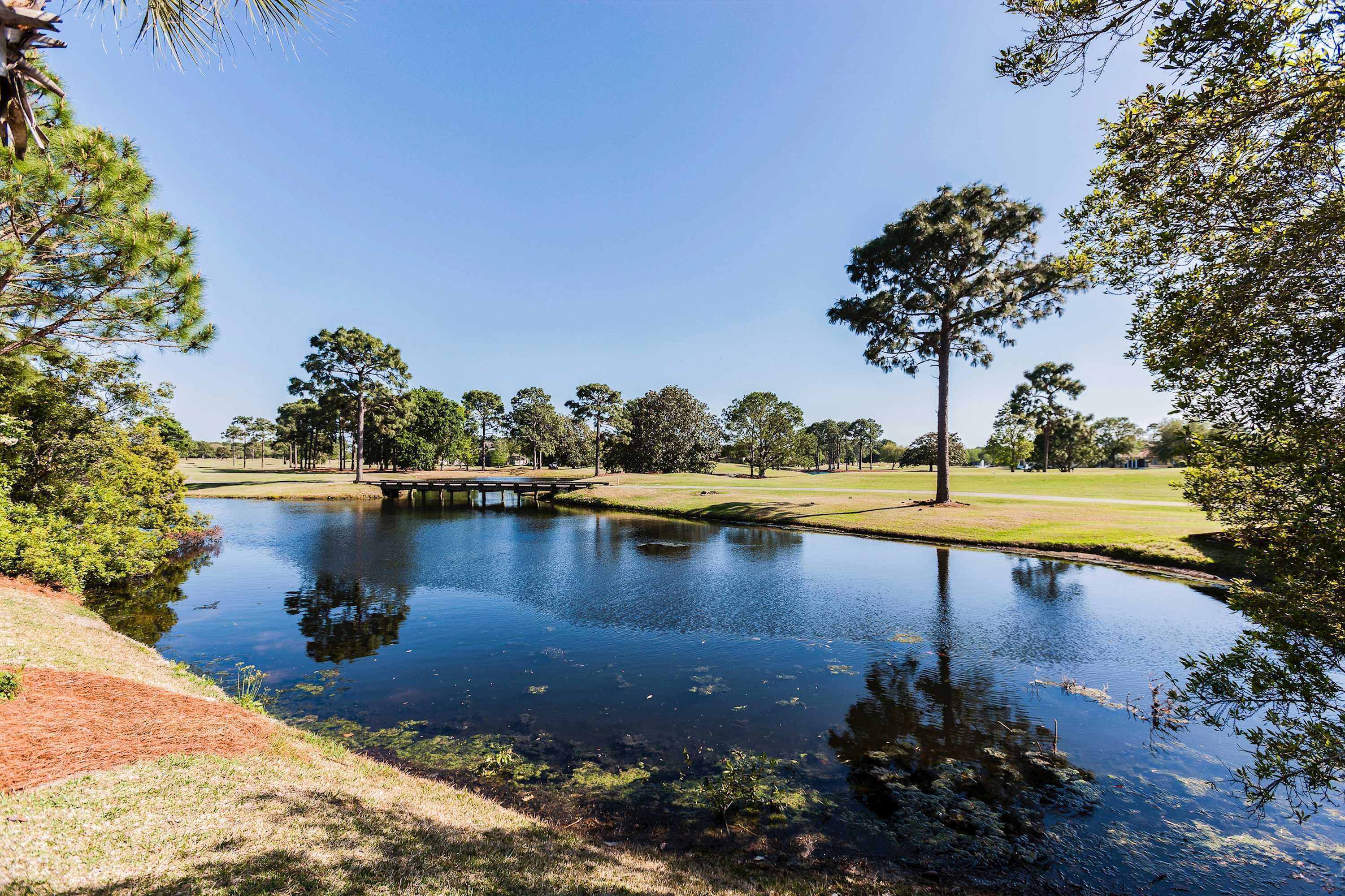 A serene landscape with a pond, trees, and a bridge.