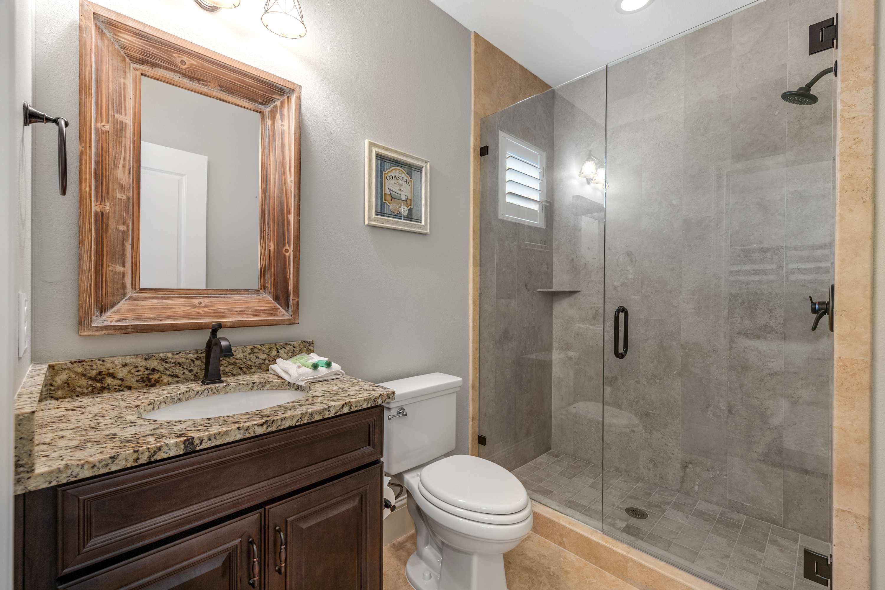 A bathroom with a granite countertop sink, a wooden vanity, a white toilet, and a glass-enclosed shower.