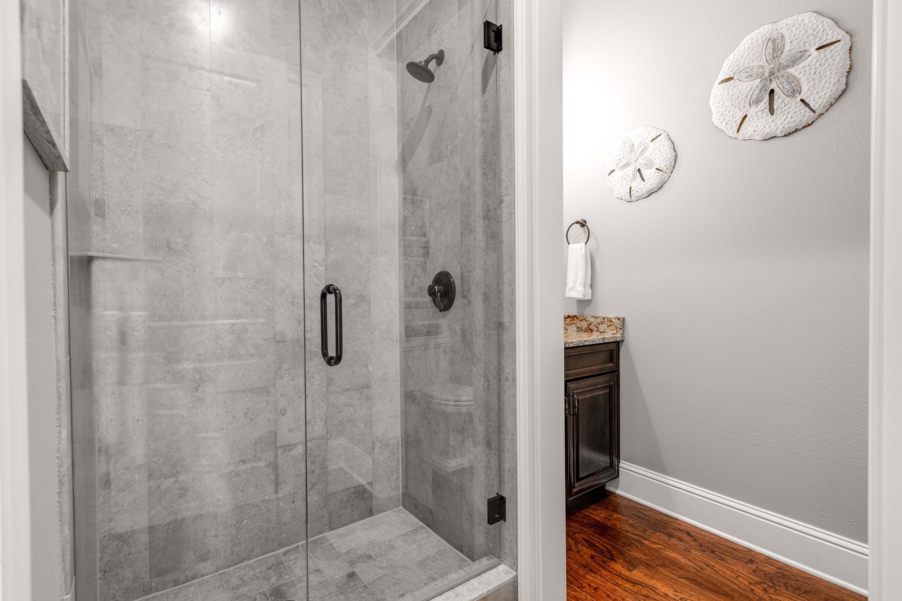 Un baño moderno con ducha de vidrio, piso de madera y tocador pequeño con aro para toalla.