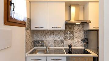 Una cocina compacta con armarios blancos, un lavamanos de acero inoxidable y azulejos decorativos en la pared.