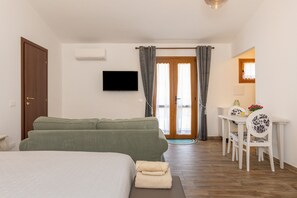 Et hotelværelse med seng, grøn sofa, spisebord med stole, fjernsyn og en dør.