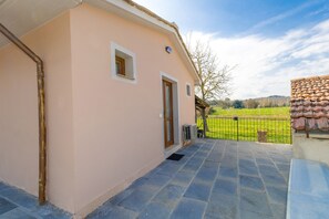 A building with a pink exterior, a tiled patio, and a view of a green field. - Apartment 'Il Mulino Del Botteghino - V' with Shared Garden, Wi-Fi & Air Conditioning (Botteghino)