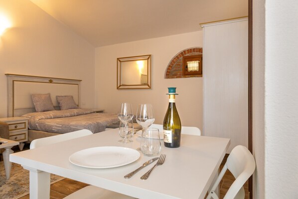 A neatly arranged dining table with a bottle of wine, glasses, and cutlery, a bed with pillows, a nightstand, and a small table with a lamp. - Apartment 'Il Mulino Del Botteghino - V' with Shared Garden, Wi-Fi & Air Conditioning (Botteghino)