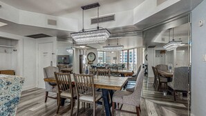 Uma sala de jantar ampla com uma grande mesa de madeira e várias cadeiras, cercada por janelas amplas que oferecem vista da cidade.