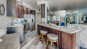 Cozinha moderna com armários de madeira escura, eletrodomésticos de aço inoxidável e uma ilha de mármore com banquetas.