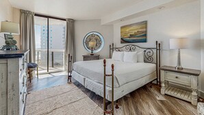 Quarto com uma cama grande, mesa de cabeceira, abajur, espelho e vista de edifícios pela janela.