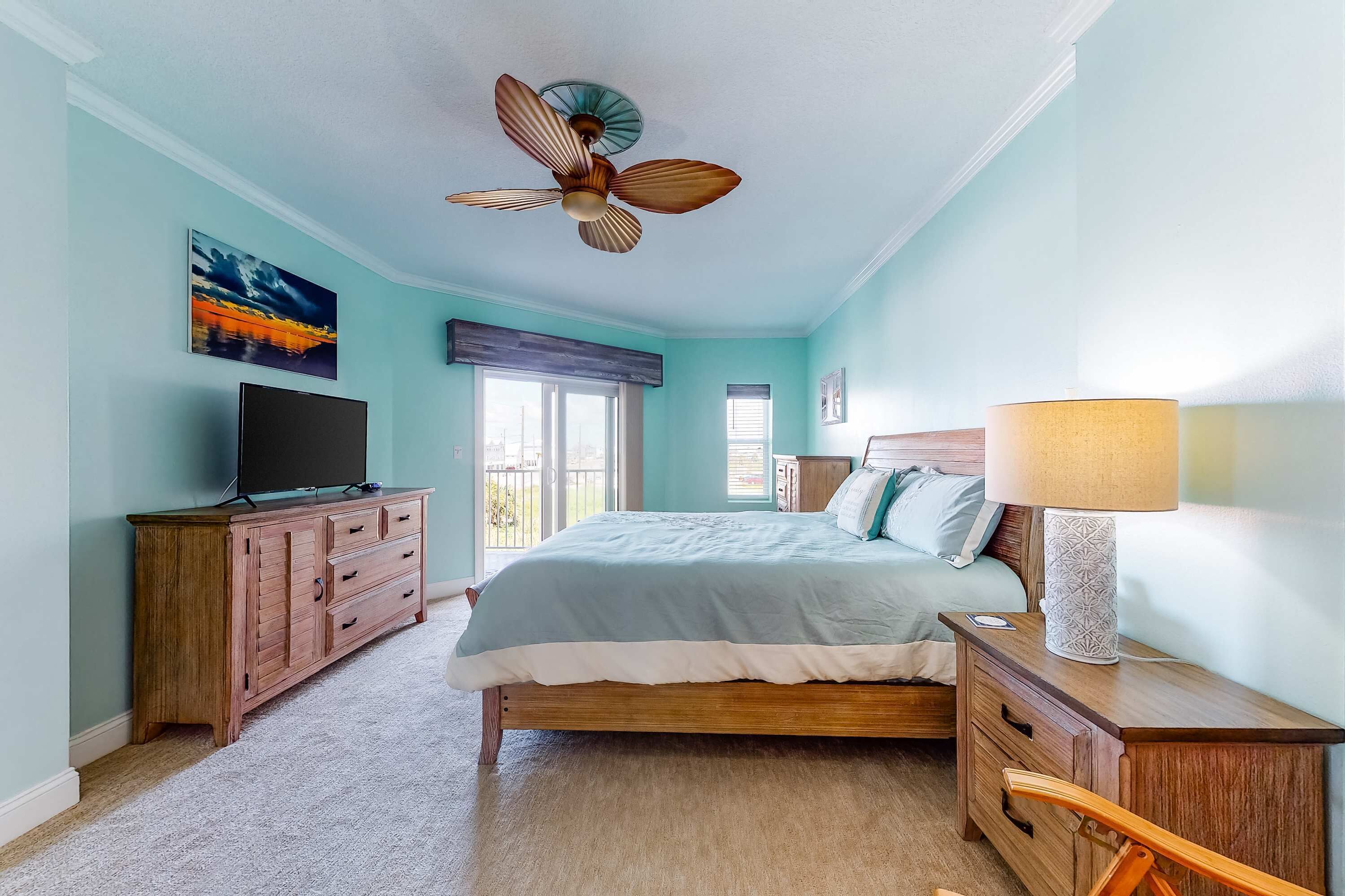 Un dormitorio con cama, cómoda de madera, televisor, ventilador de techo y ventana.